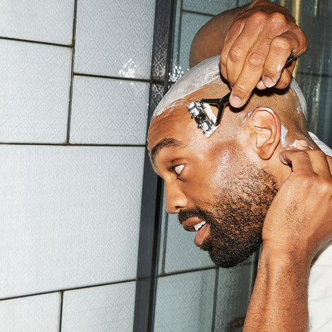 male shaving his head, smiling, with a leaf razor